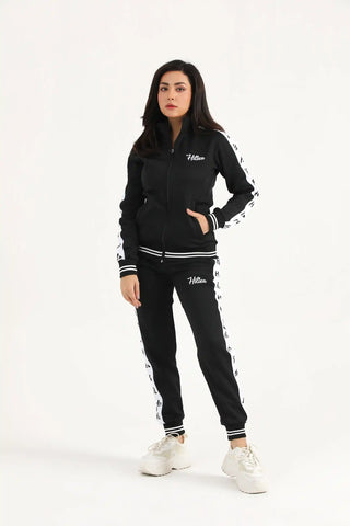 Full-length view of a woman wearing a black Hilton Aesthetics zip-up jacket and matching joggers