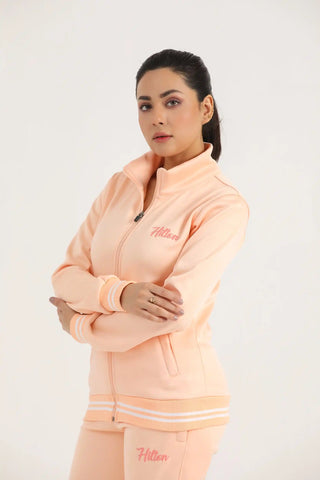Woman modelling a peach athletic zip-up jacket with embroidered chest logo, angled view