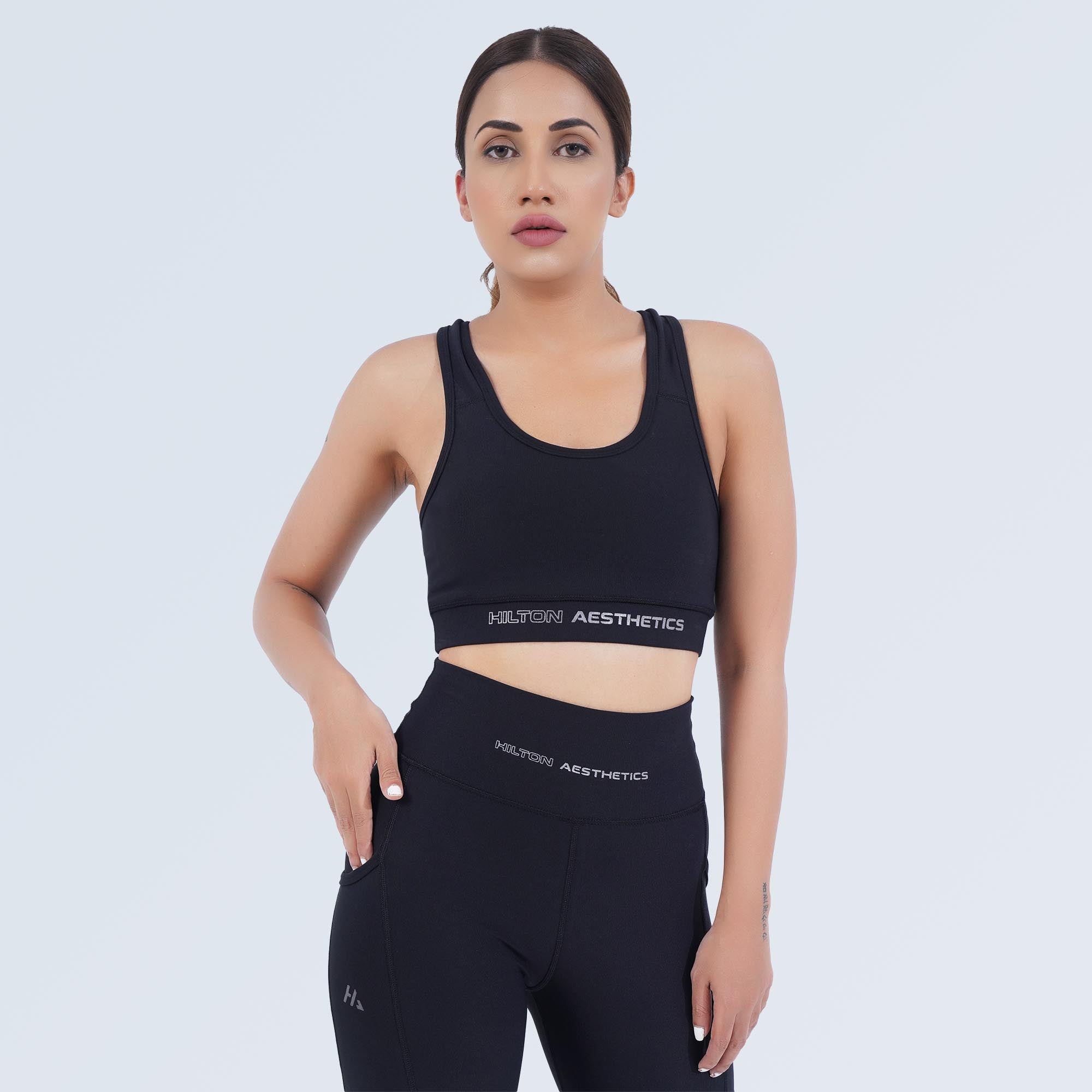 Front view of a model wearing the black Impact Sports Bra by Hilton Aesthetics with matching leggings