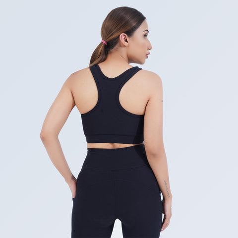 Back view of a model wearing the black Impact Sports Bra by Hilton Aesthetics with matching leggings