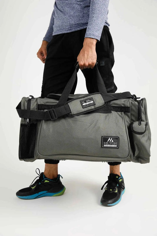 Man carrying grey Hilton Aesthetics Essential Duffel Bag, side view